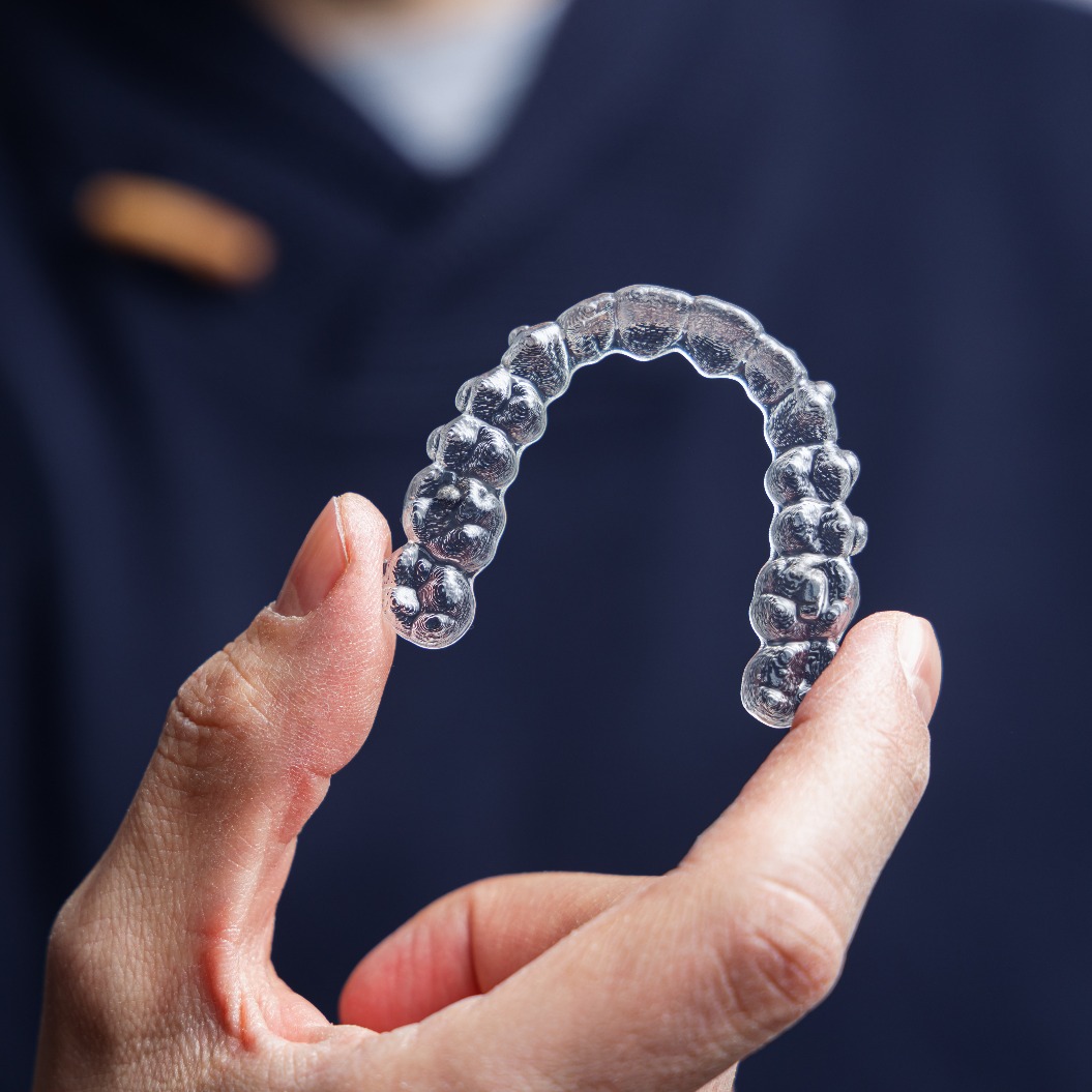 Ein Mann, der eine durchsichtige Zahnschiene in der Hand hält. Invisalign-Kieferorthopädie –