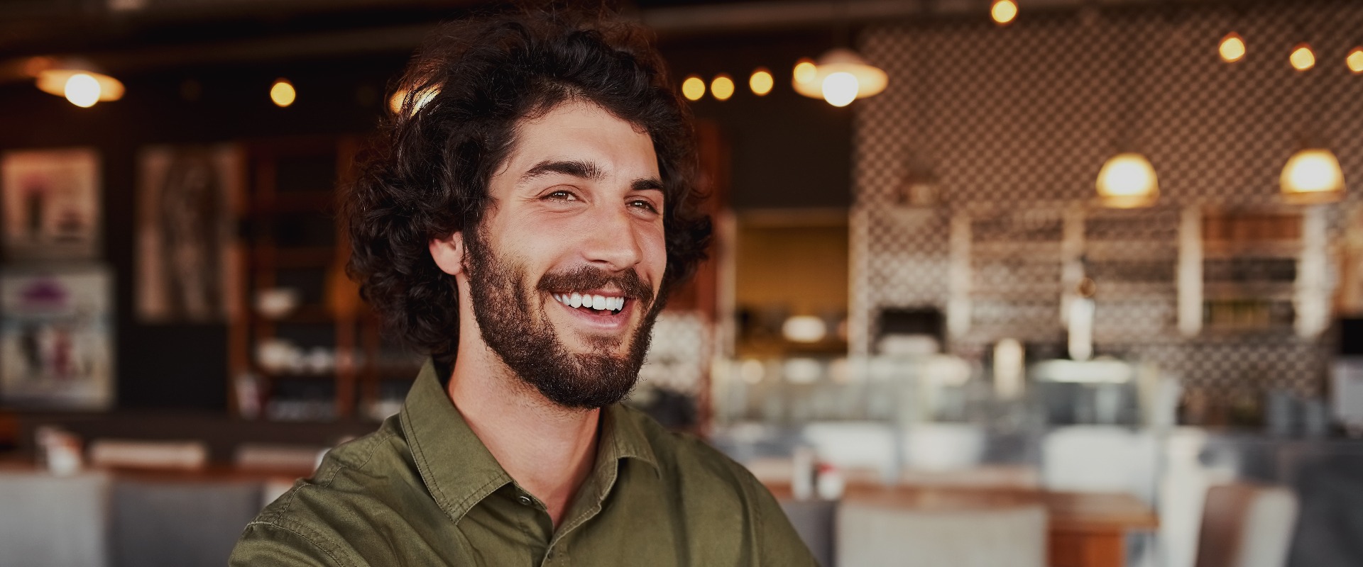 Porträt eines gutaussehenden jungen Mannes, der in seiner Freizeit in einem modernen Café sitzt und lacht, während er eine lustige Nachricht auf seinem Handy liest
