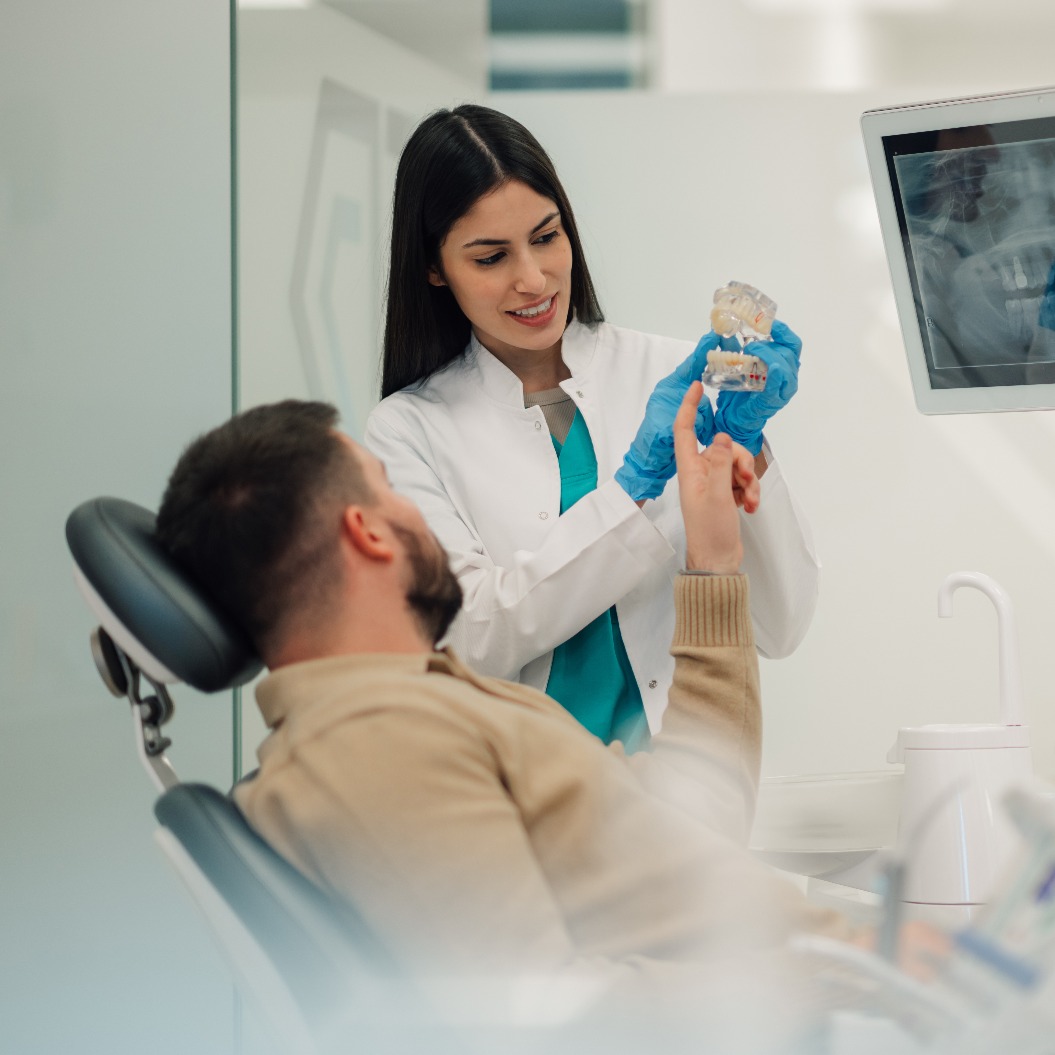 Zahnärztin, die einem Patienten in einer modernen Praxis ein Zahnmodell zeigt